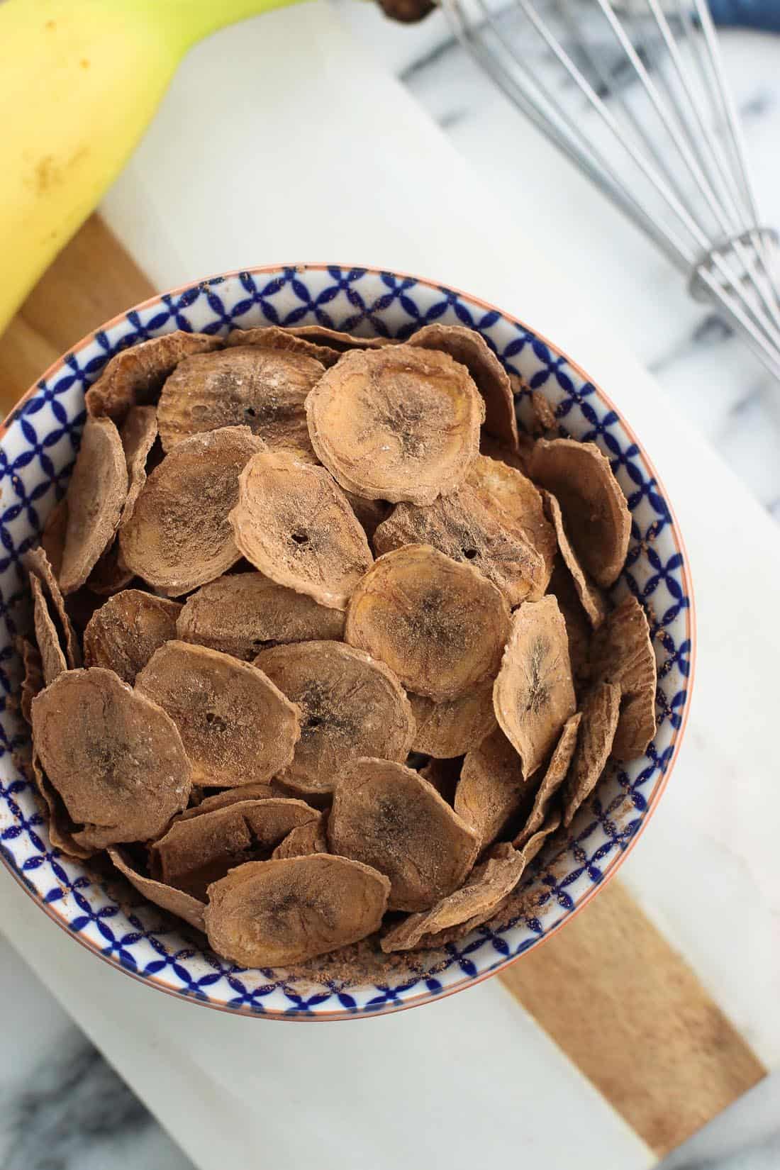 An overhead shot of banana chips in a small bowl on a marble board