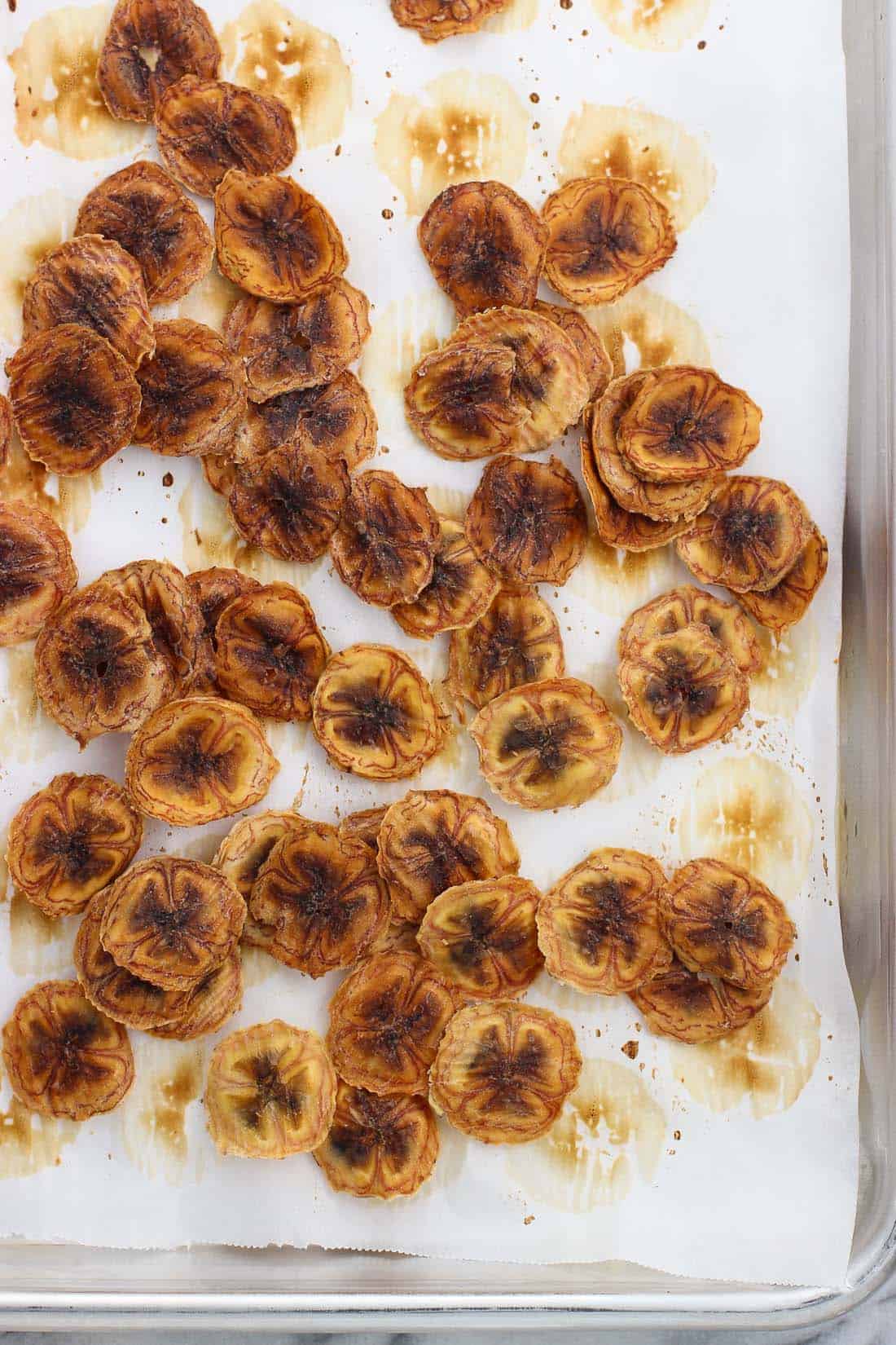 Banana chips on a parchment paper lined metal baking sheet