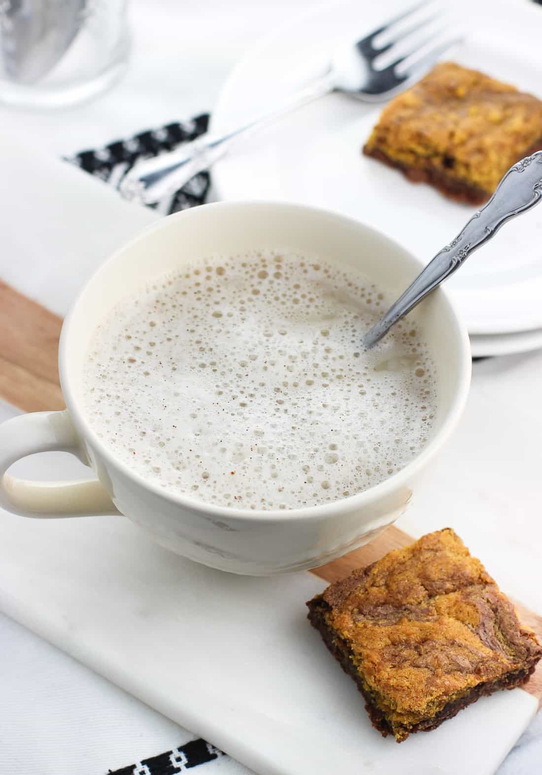 A spoon stirred into a chamomile tea latte on a tray next to a brownie.