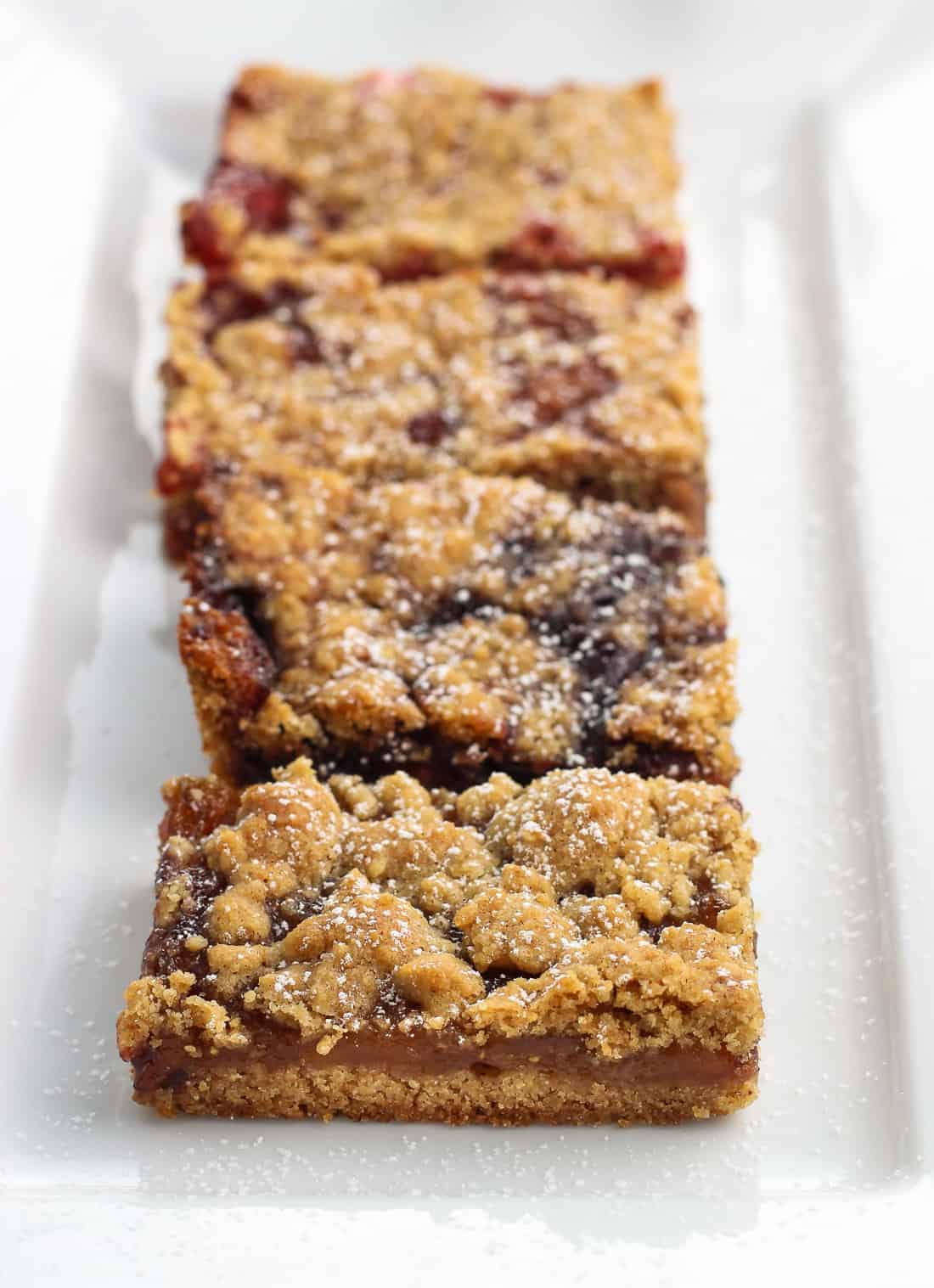 A line-up of four different flavors of jam bars on a rectangular ceramic serving tray