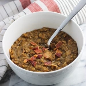 A bowl of lentil soup topped with crumbled bacon with a spoon in it.