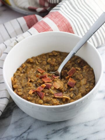 A bowl of thick lentil soup with bacon and a spoon.