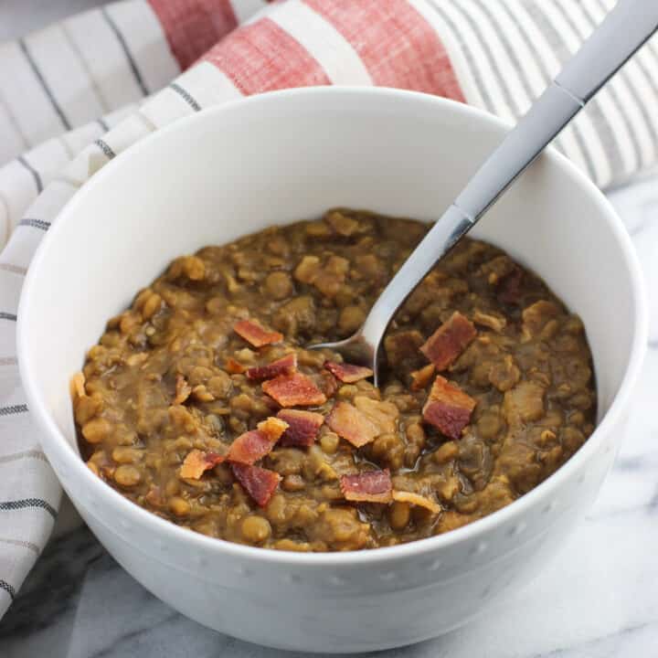 A bowl of thick lentil soup with bacon and a spoon.