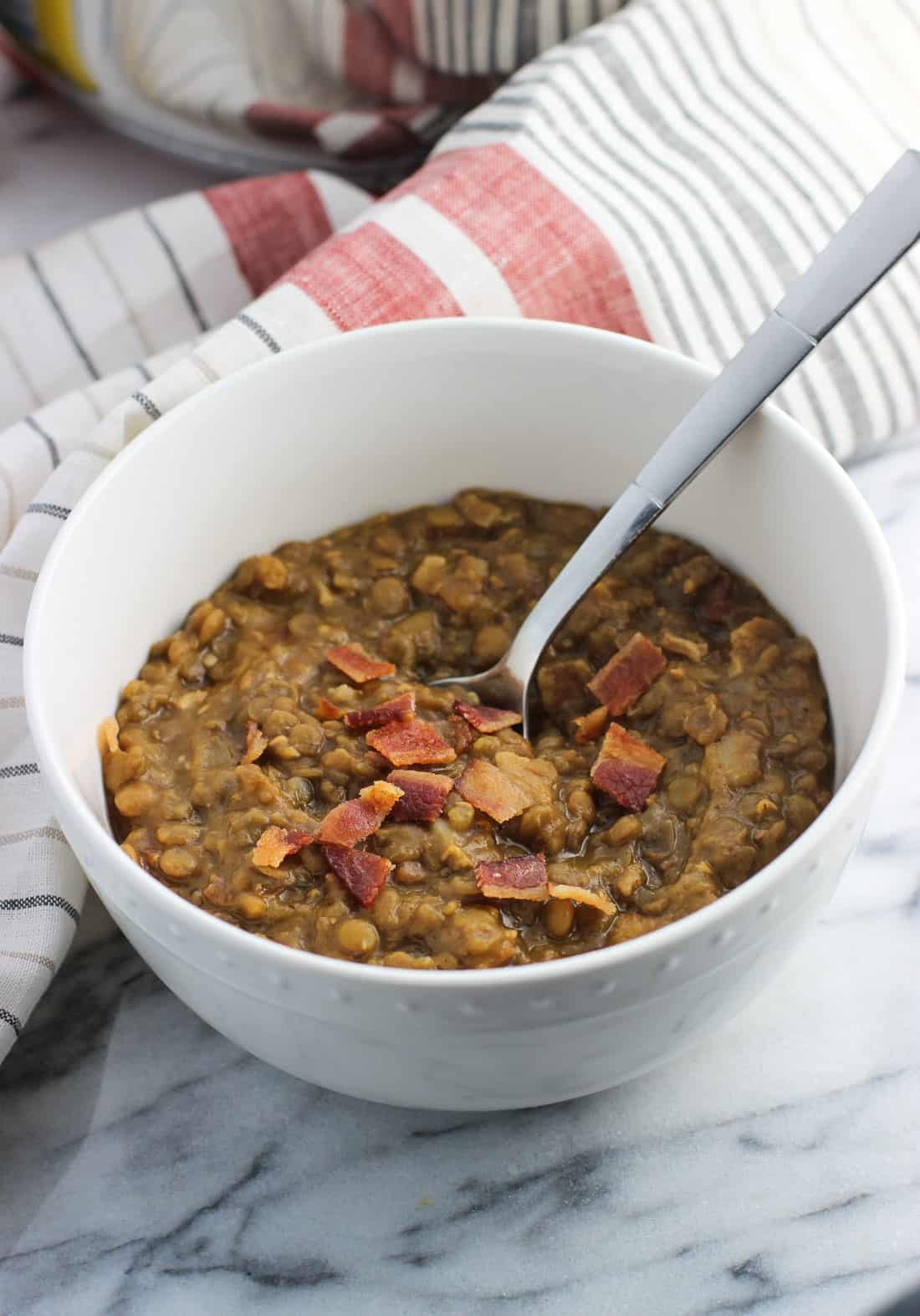 A bowl of thick lentil soup with bacon and a spoon.