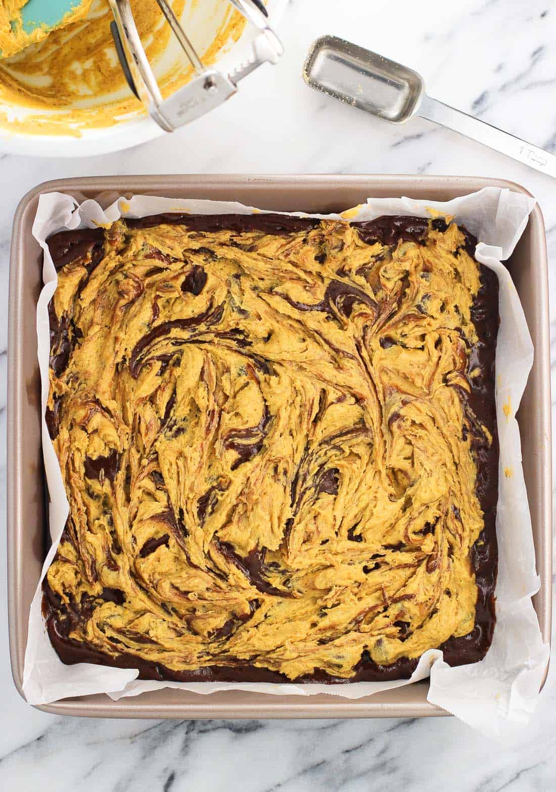 An overhead view of the brownies with a pumpkin swirl layer in the pan before being baked