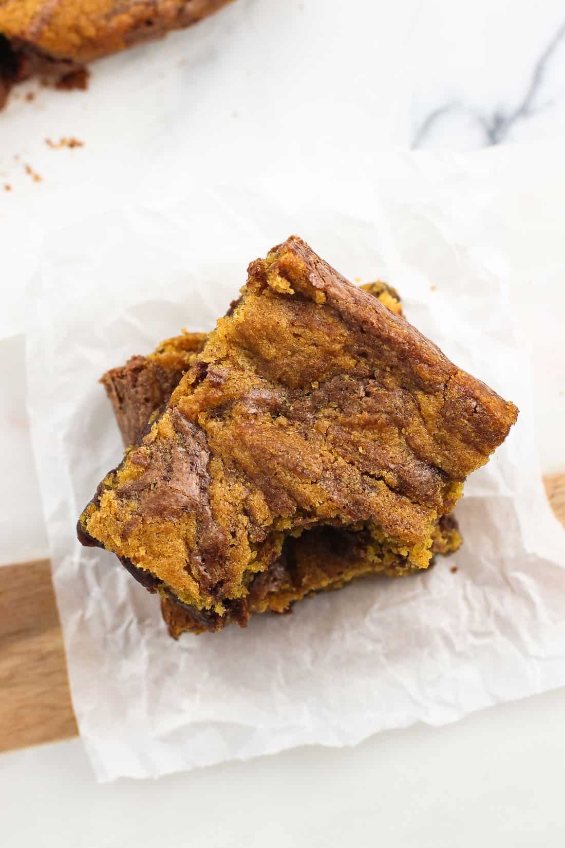 An overhead shot of two brownies stacked on top of one another on crinkled parchment paper.