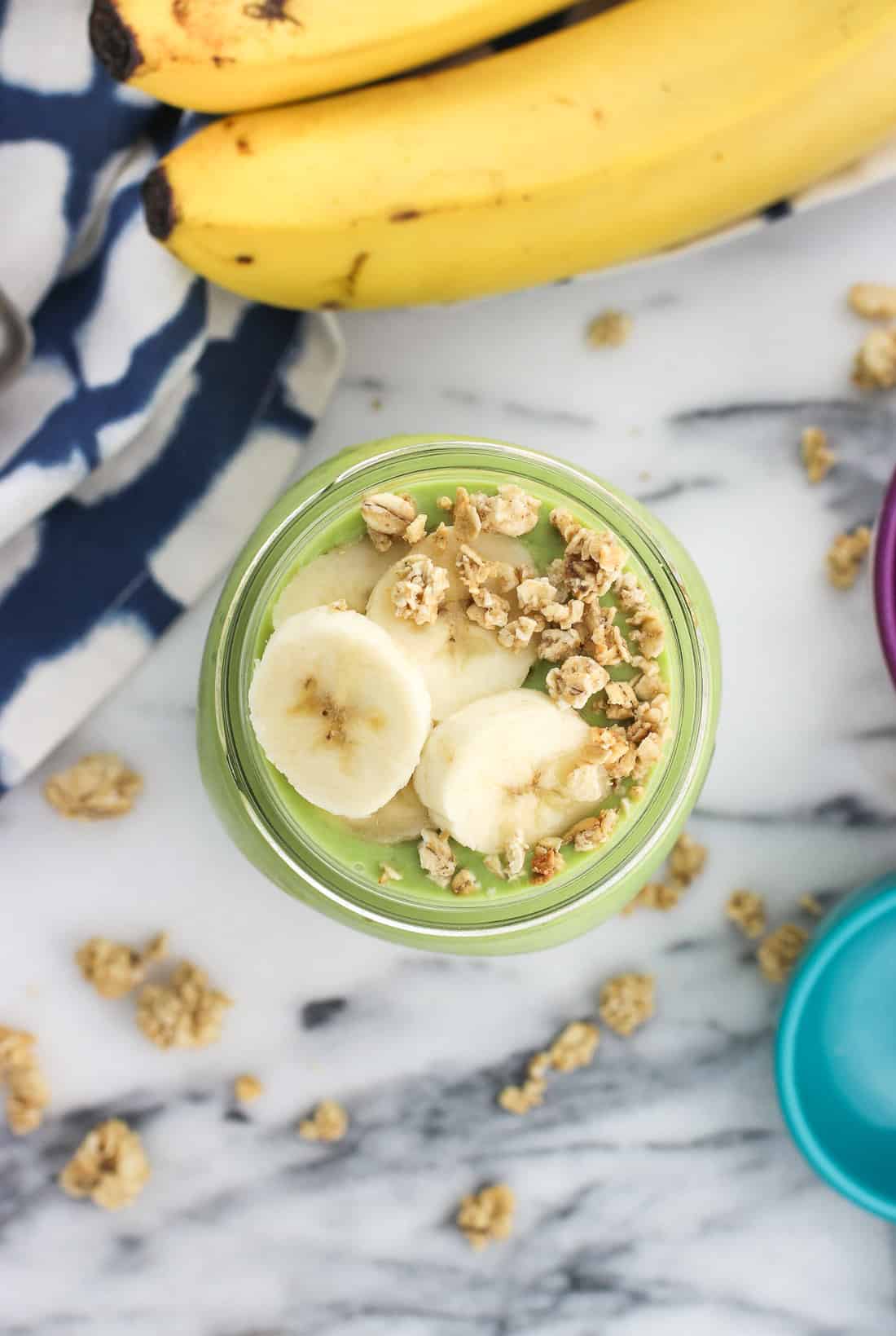 An overhead picture of a smoothie topped with banana slices and granola clusters