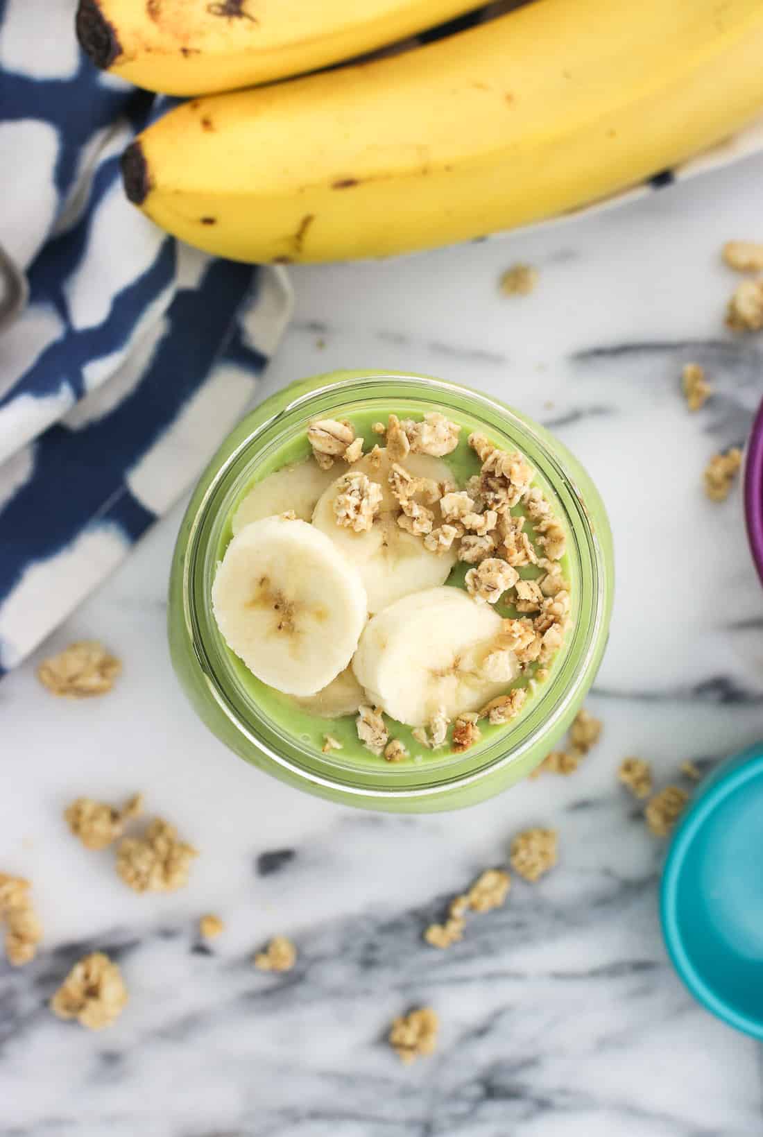 An overhead picture of a smoothie topped with banana slices and granola clusters