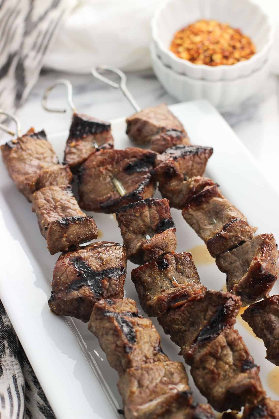 Three skewers of beef with a small bowl of dry seasoning in the background