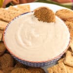 A bowl of yogurt dip on a plate with graham crackers and gingersnap cookies with a gingersnap dunked in