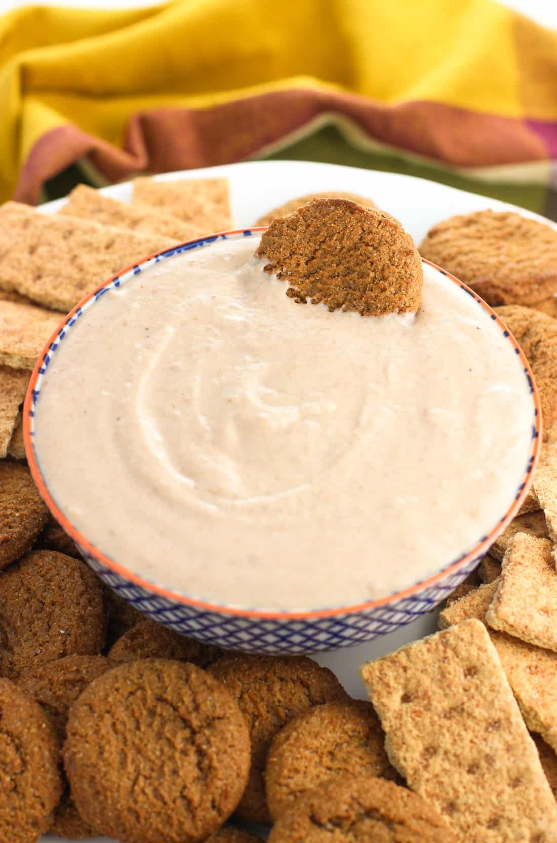 A bowl of yogurt dip on a plate with graham crackers and gingersnap cookies with a gingersnap dunked in