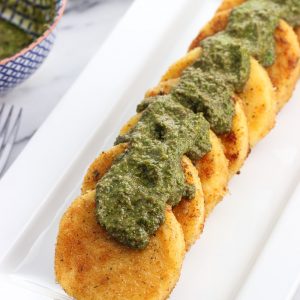 Polenta slices on a serving tray with dollops of basil pesto over top