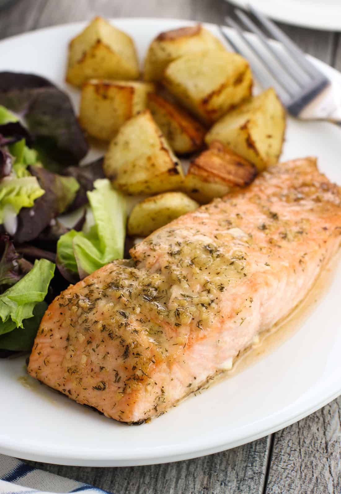 A dinner plate of a salmon fillet coated in horseradish sauce, roasted potato cubes, and a side salad