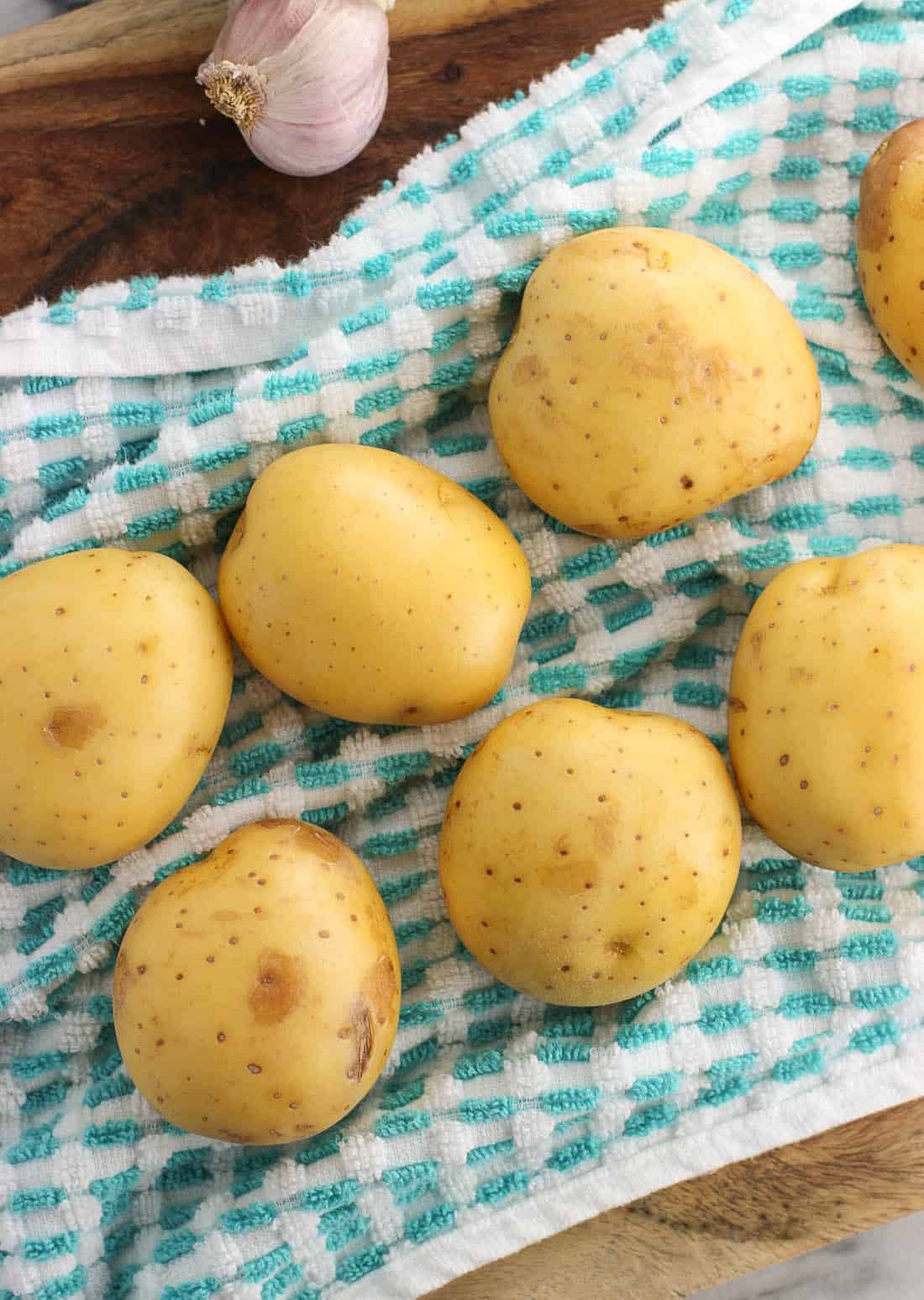 Seven scrubbed yellow potatoes on a dish towel next to a head of garlic