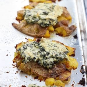 Spinach artichoke dip dolloped on top of smashed potatoes on a metal baking sheet