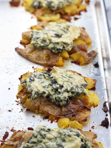 Spinach artichoke dip dolloped on top of smashed potatoes on a metal baking sheet