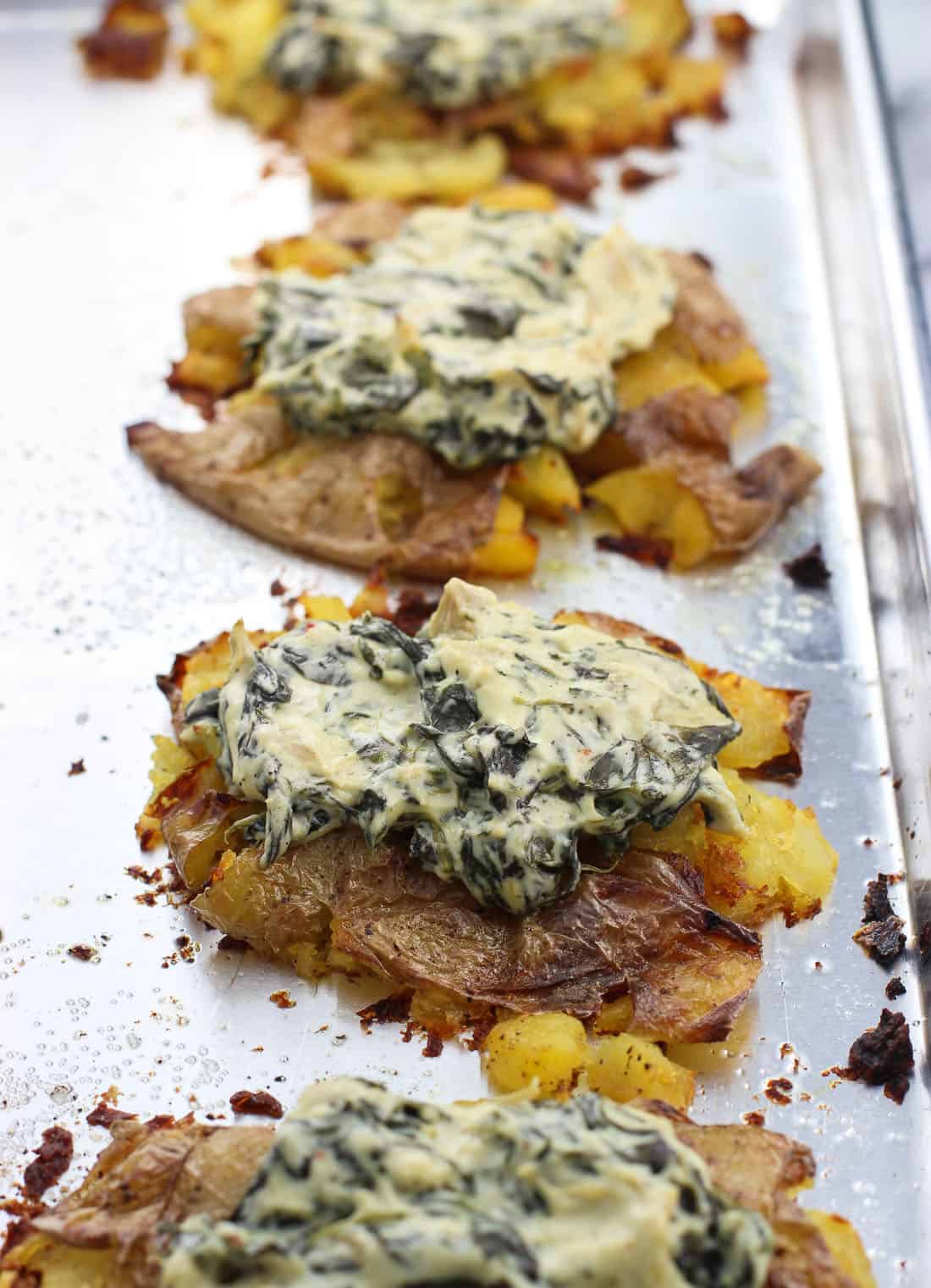 Spinach artichoke dip dolloped on top of smashed potatoes on a metal baking sheet