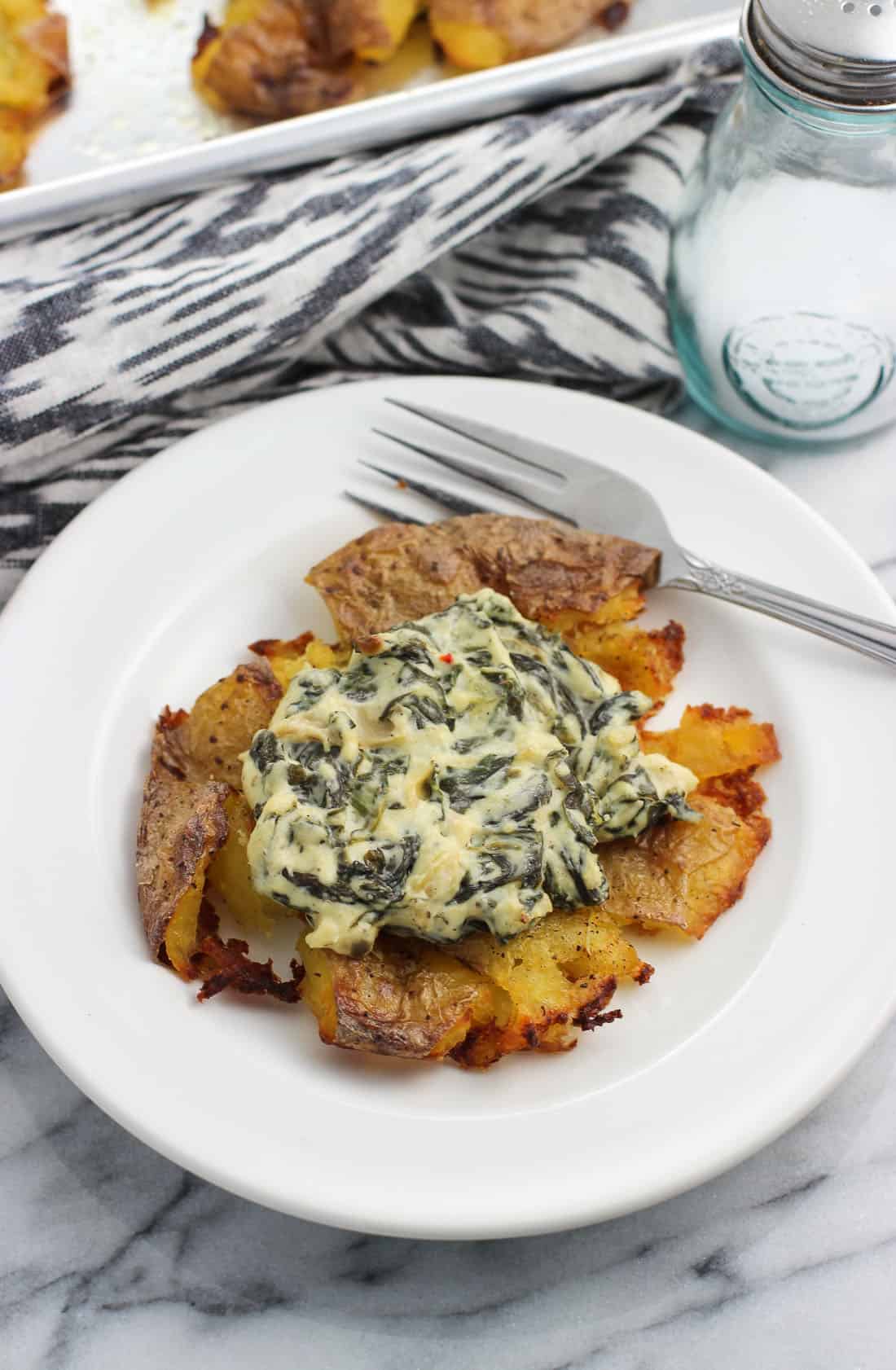 A smashed potato on a small appetizer plate topped with spinach artichoke dip