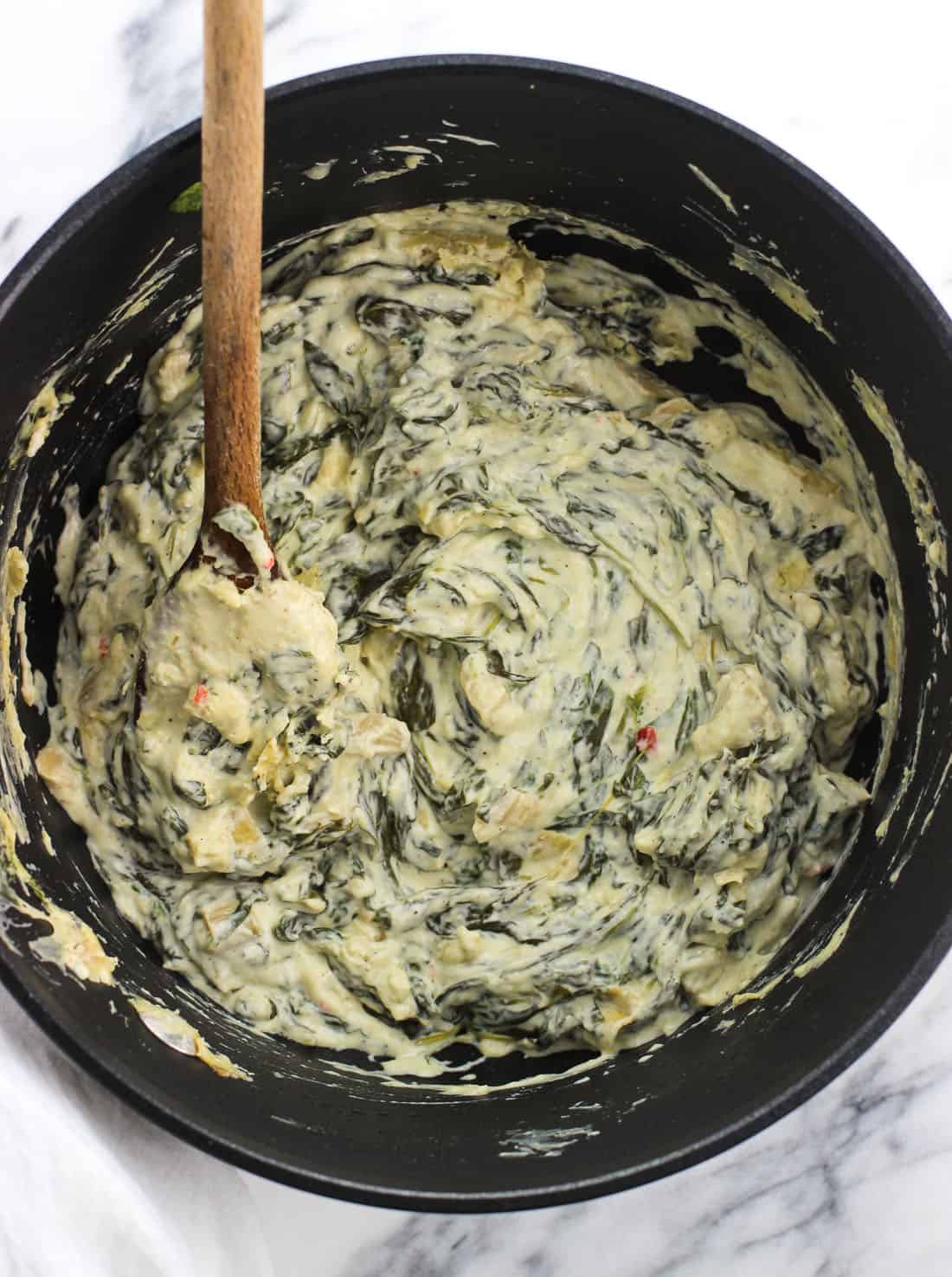 A medium saucepan filled with spinach artichoke dip with a wooden spoon