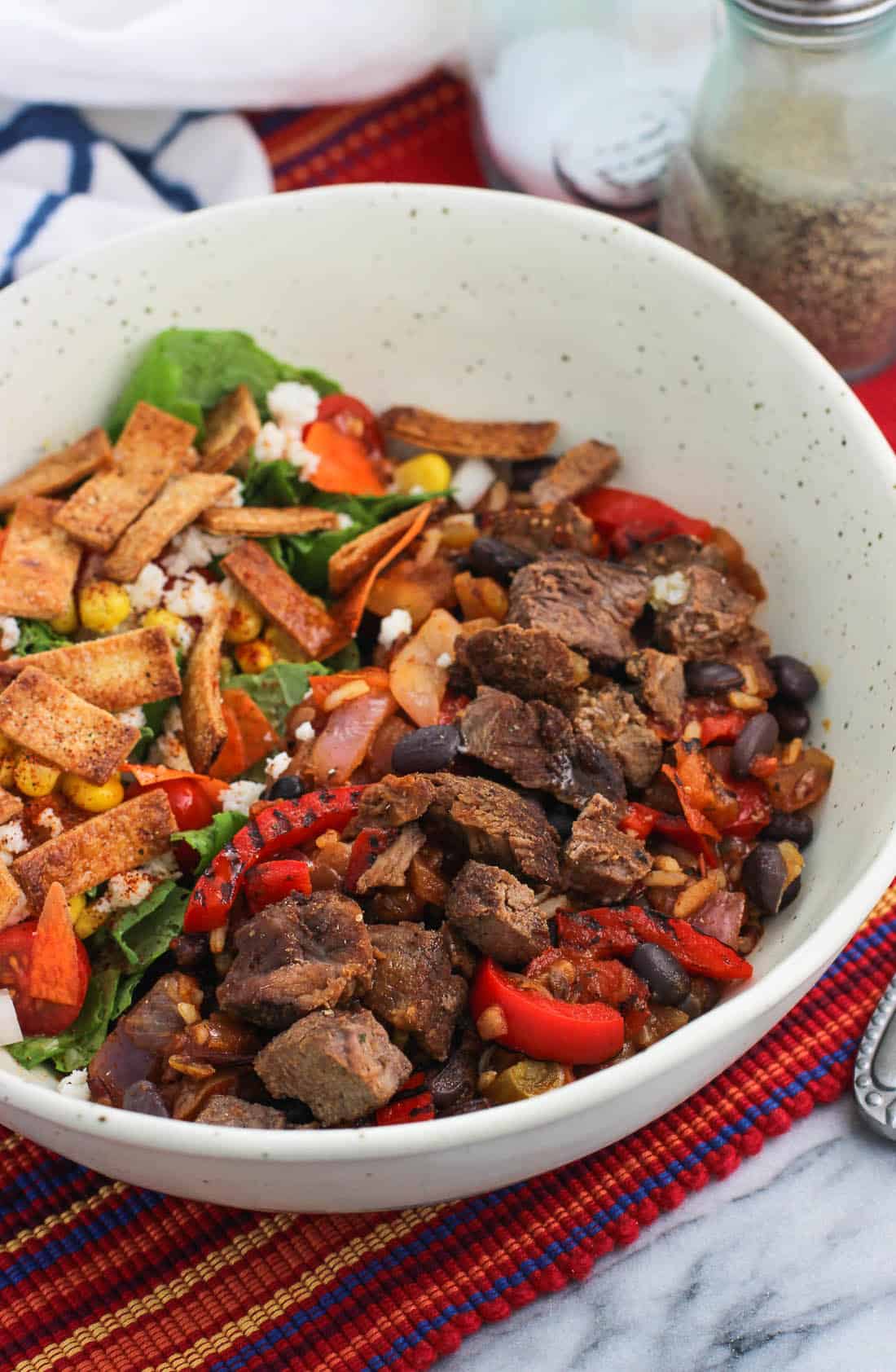 Barbacoa beef and peppers in a bowl next to a salad with salt and pepper shakers in the background