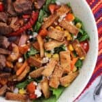 A side salad topped with tortilla strips in a bowl with steak and peppers
