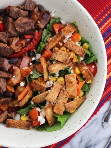 A side salad topped with tortilla strips in a bowl with steak and peppers