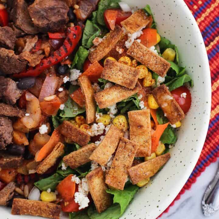 A side salad topped with tortilla strips in a bowl with steak and peppers