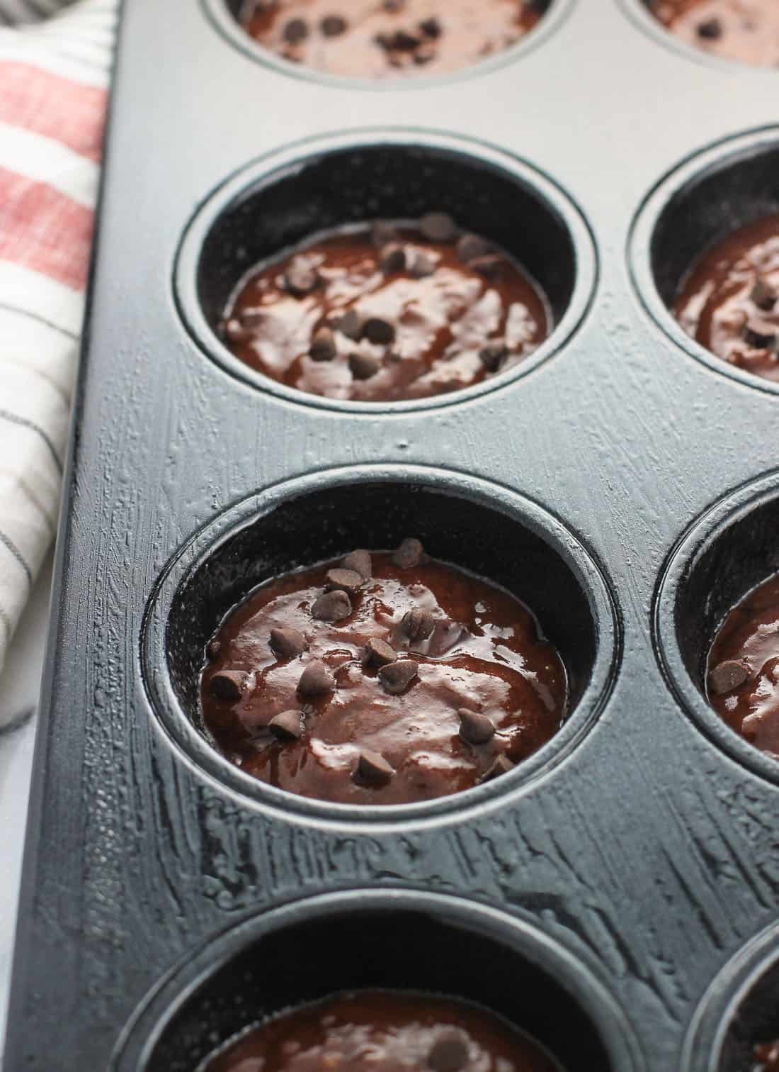 Muffin batter topped with mini chocolate chips portioned out into a regular-sized muffin tin