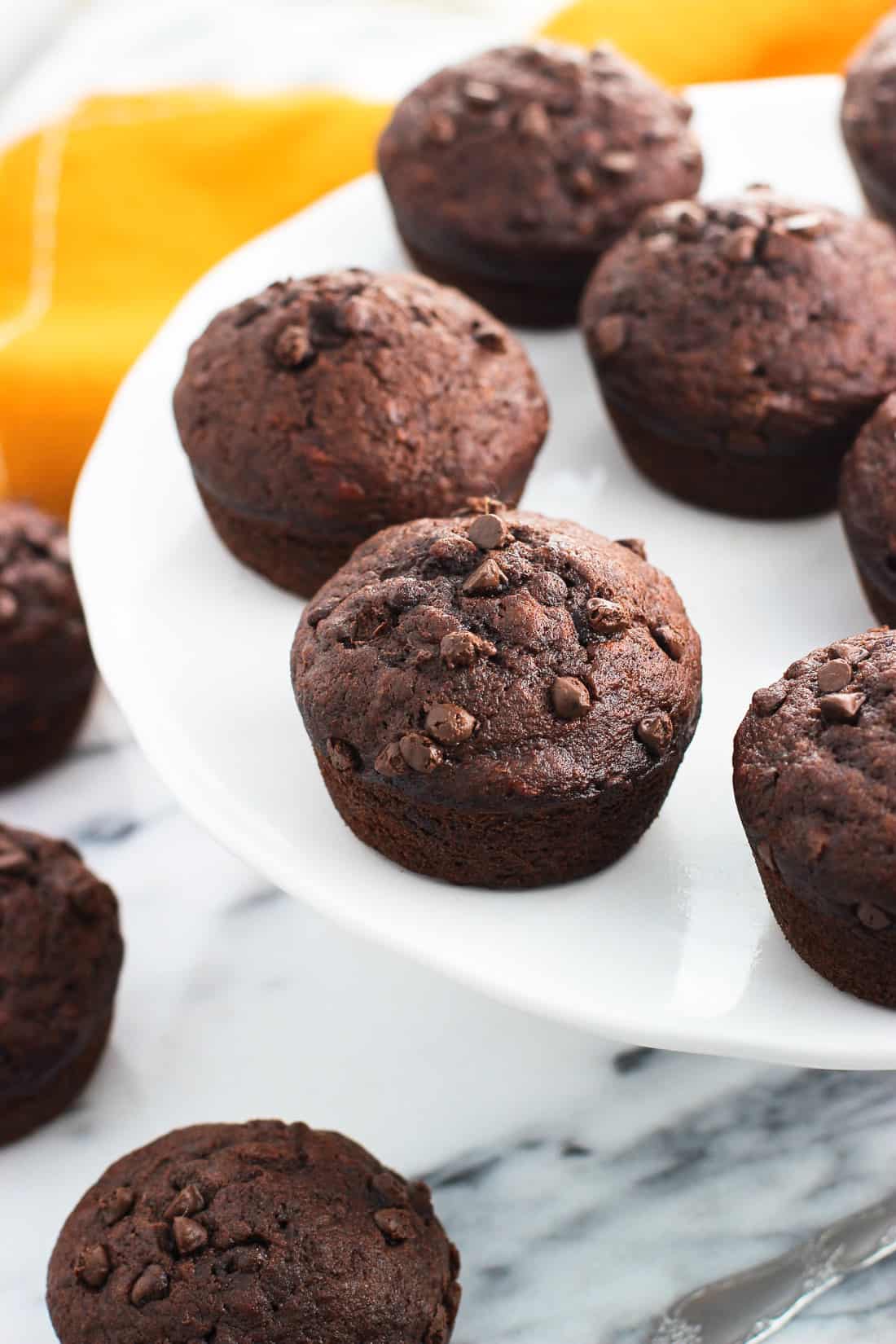 Whole muffins displayed on a ceramic cake stand set on a marble board