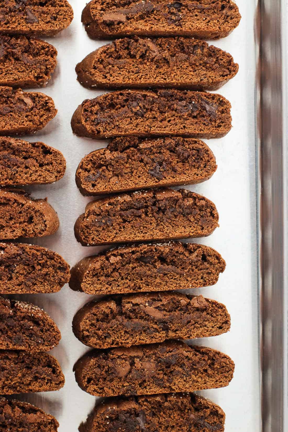 Biscotti on their sides lined up, one on top of the other, on a metal baking sheet