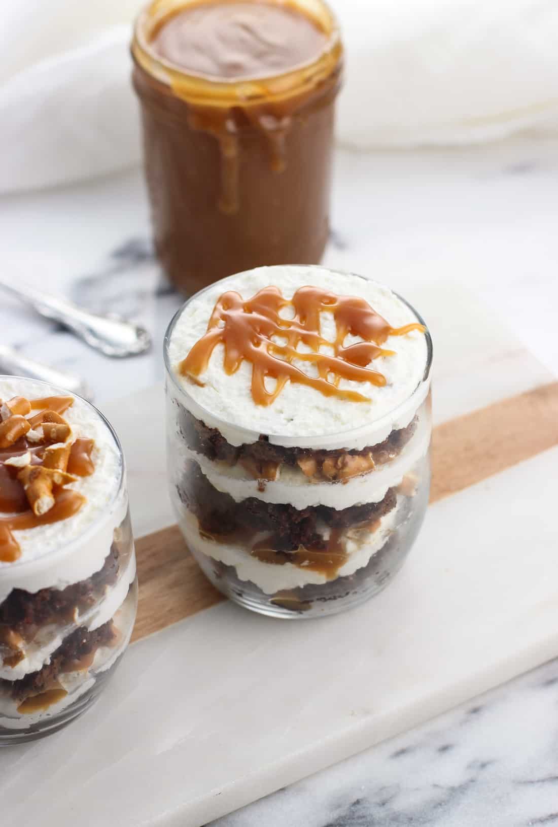 Two brownie trifles in small glasses next to a jar of caramel sauce.