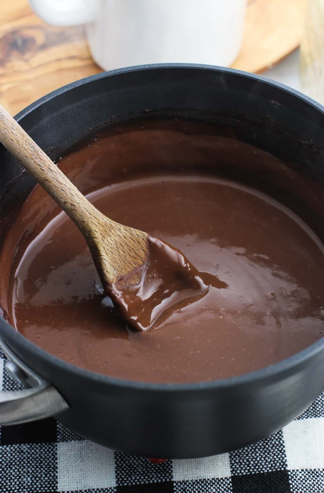The mocha hot chocolate mixture in a sauce pan with a thickly-coated wooden spoon in it.