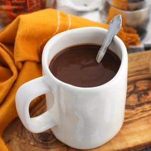 A large mug of hot chocolate with a spoon in it on a wooden tray.