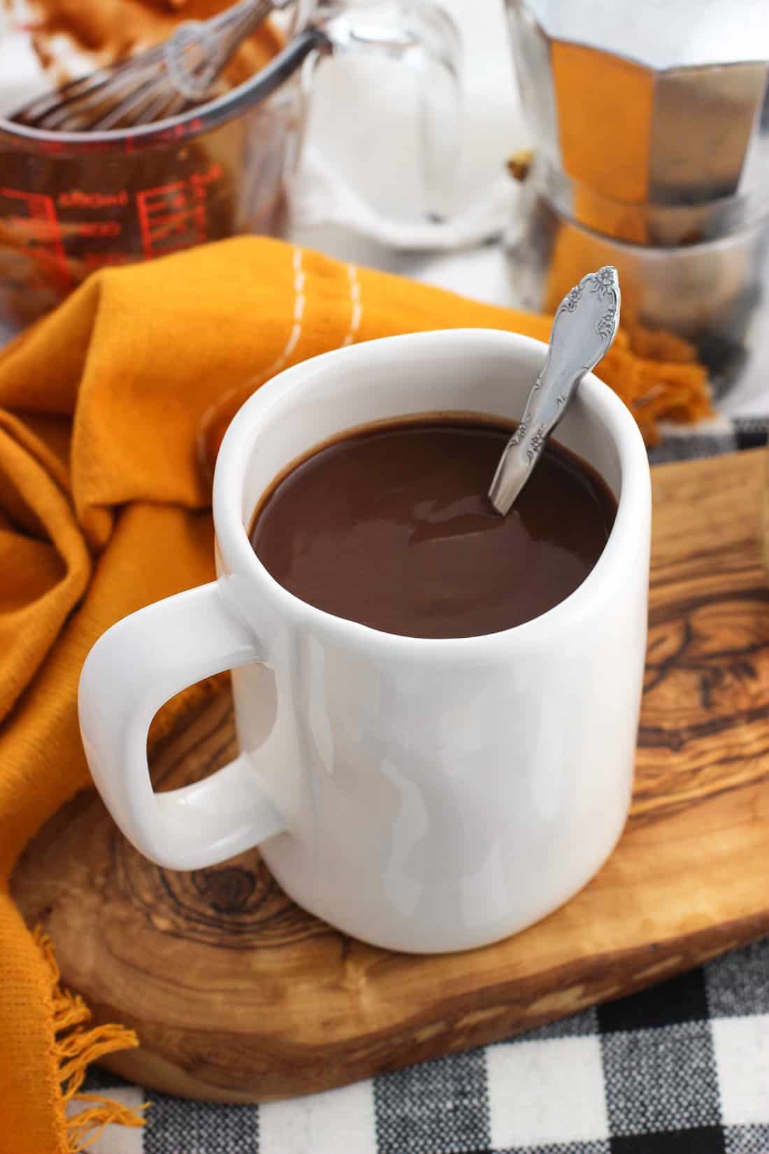 A large mug of hot chocolate with a spoon in it on a wooden tray.