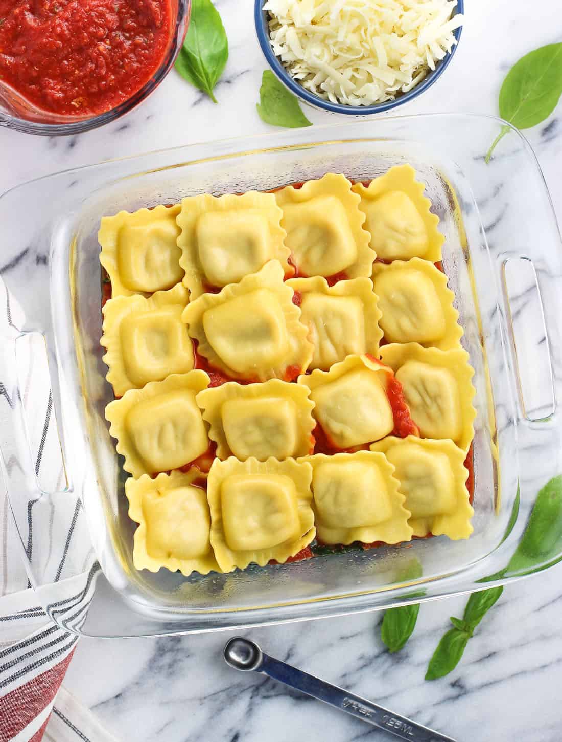 An overhead picture of ravioli in a square glass baking dish nestled on top of spinach and marinara sauce before adding the rest of the ingredients.