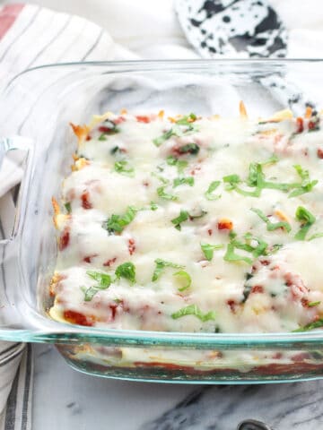 A glass baking dish filled with spinach, ravioli and marinara sauce, topped with melted mozzarella and fresh basil