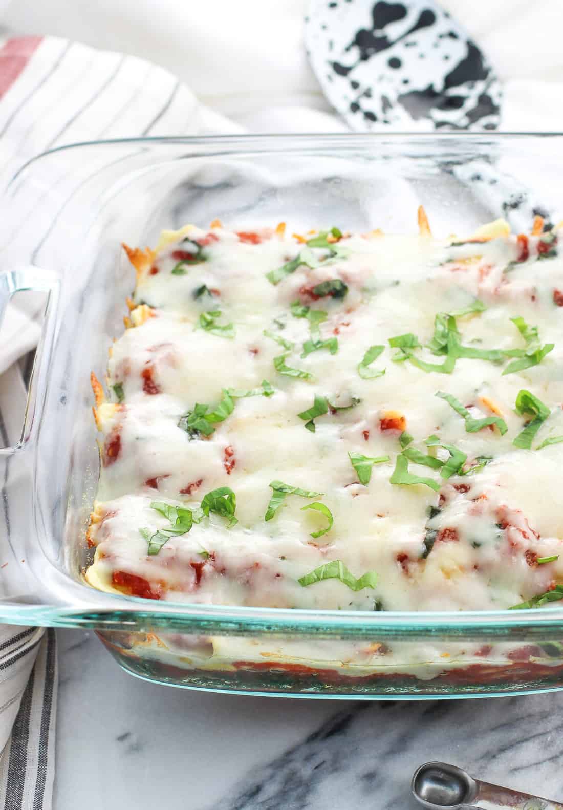 A glass baking dish filled with spinach, ravioli and marinara sauce, topped with melted mozzarella and fresh basil.