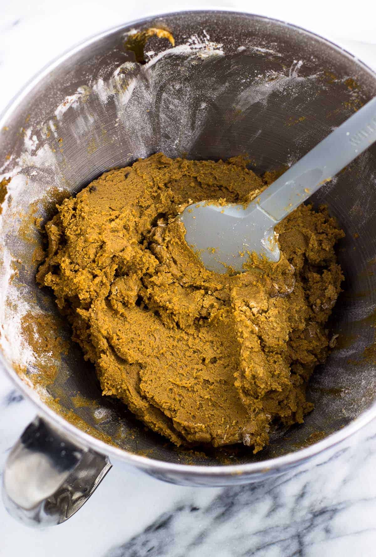 Cookie dough with a spatula in a metal stand mixer bowl before chilling.