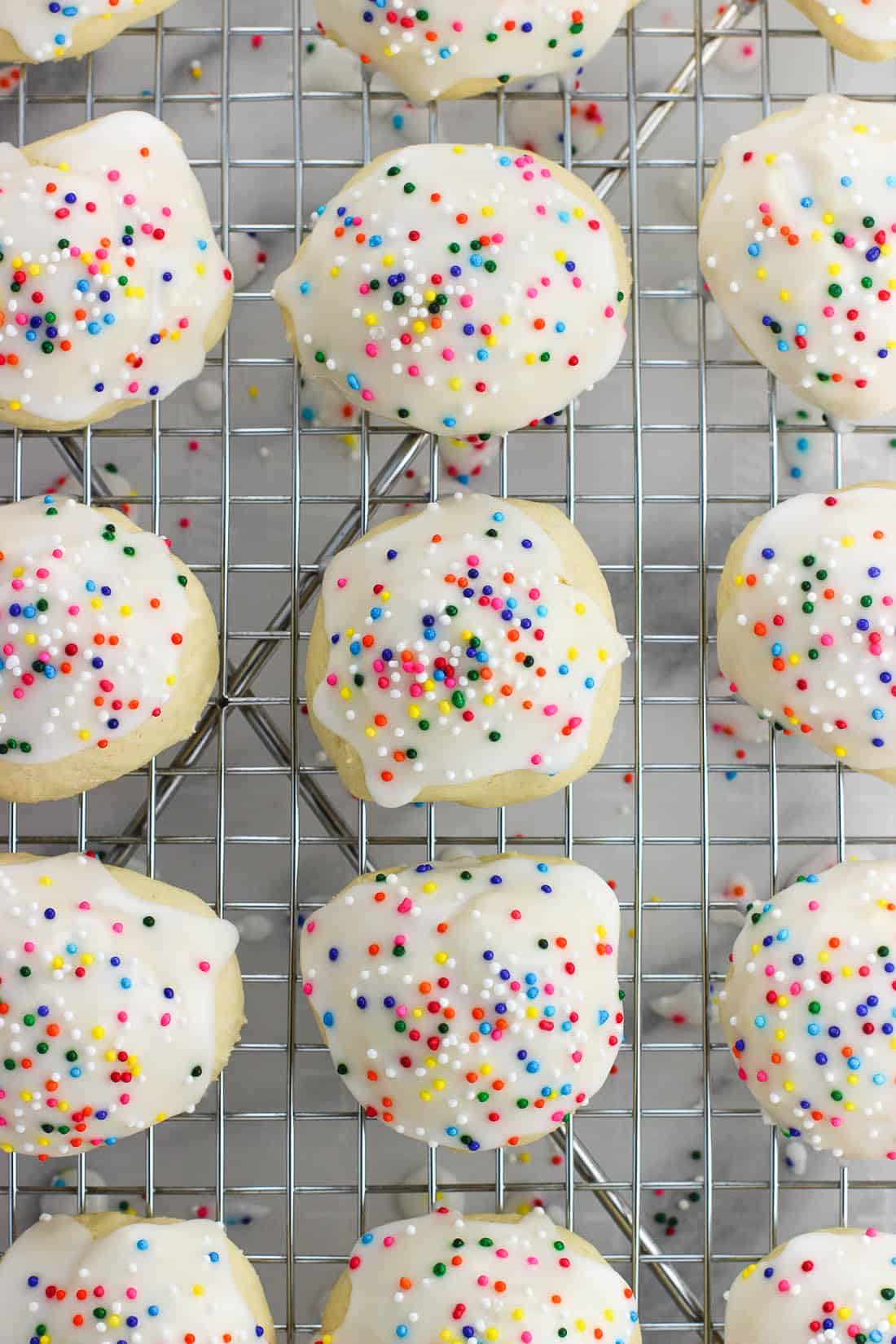 Glazed and sprinkled anise cookies on a wire rack.