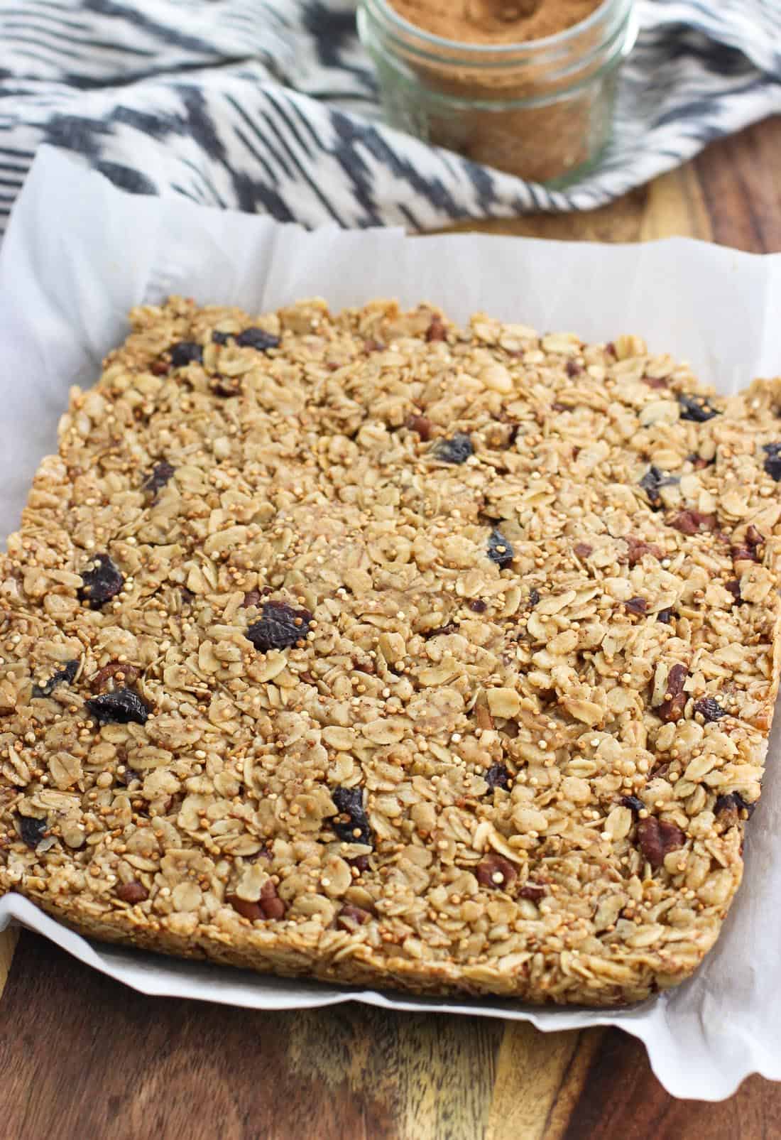 An 8" x 8" slab of granola bar mixture on a wooden board before being cut into slices