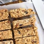 Sliced granola bars on a wooden cutting board next to a jar of pumpkin pie spice