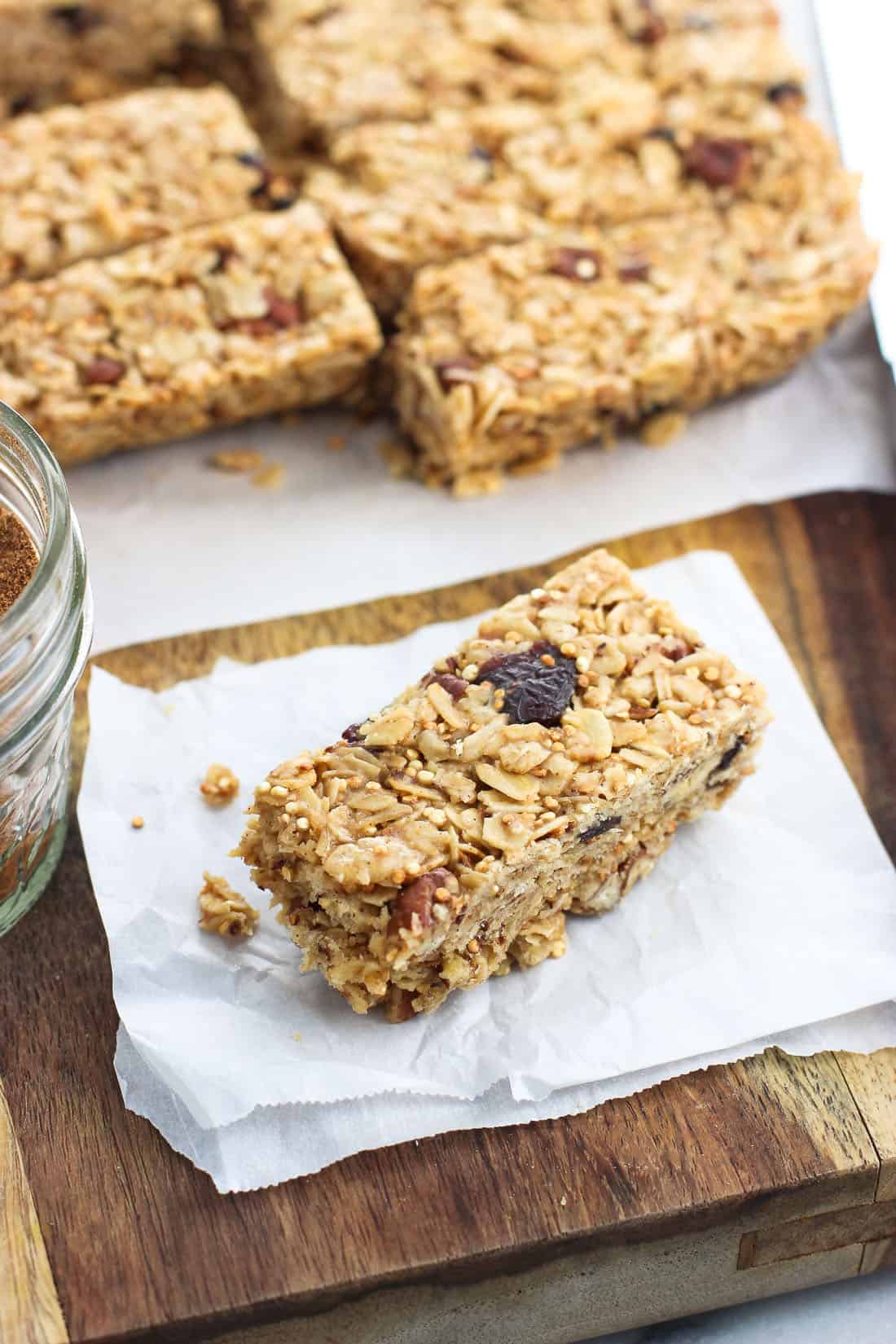 A close-up of a granola bar with a few bites taken out of it resting on a small piece of parchment paper with the rest of the bars in the background