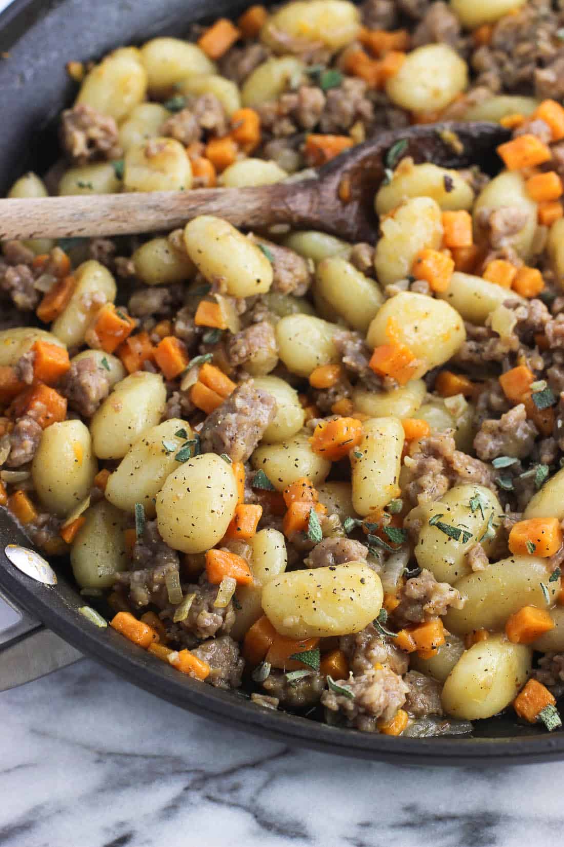 Gnocchi, sausage, and sweet potato mixed together in a skillet with a spoon.