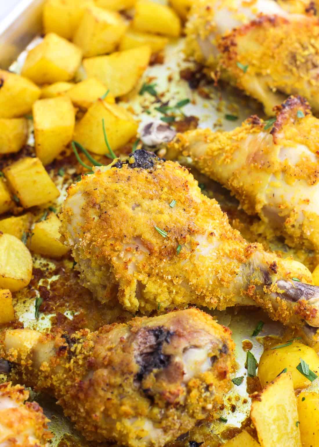 Breadcrumb-coated chicken drumsticks and potato cubes on a metal sheet pan after cooking