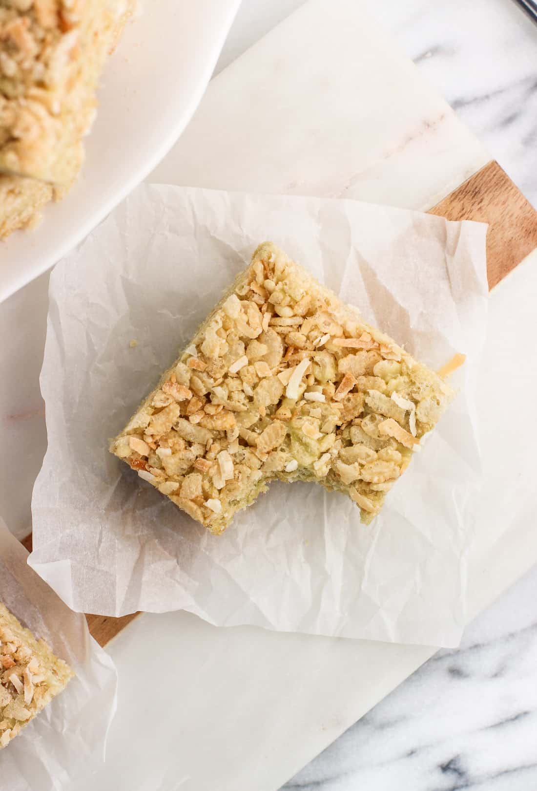 A matcha rice crispy treat with a big bite taken out of it on a piece of parchment paper.