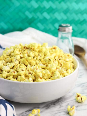 A serving bowl of turmeric popcorn next to a shaker of salt