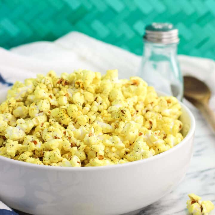 A serving bowl of turmeric popcorn next to a shaker of salt