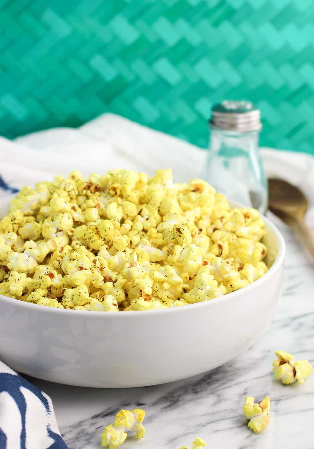 A shallow serving bowl of turmeric popcorn in front of a salt shaker
