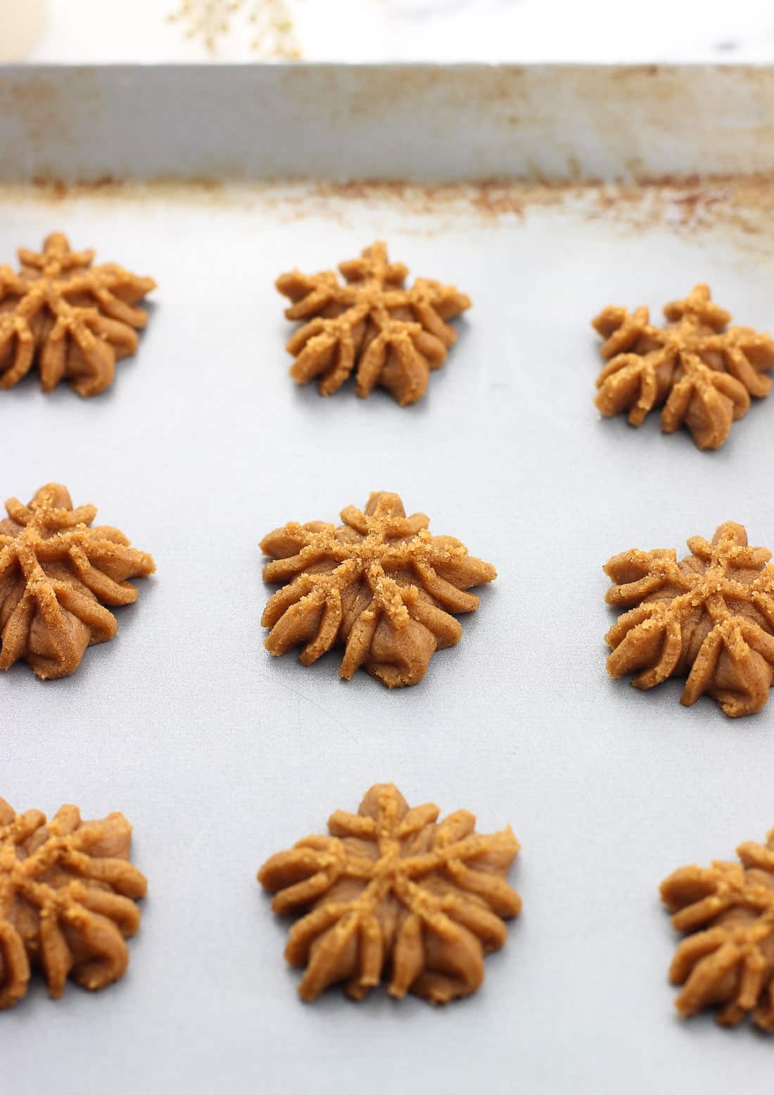 Snowflake-shaped cookies on a metal cookie sheet before being baked.