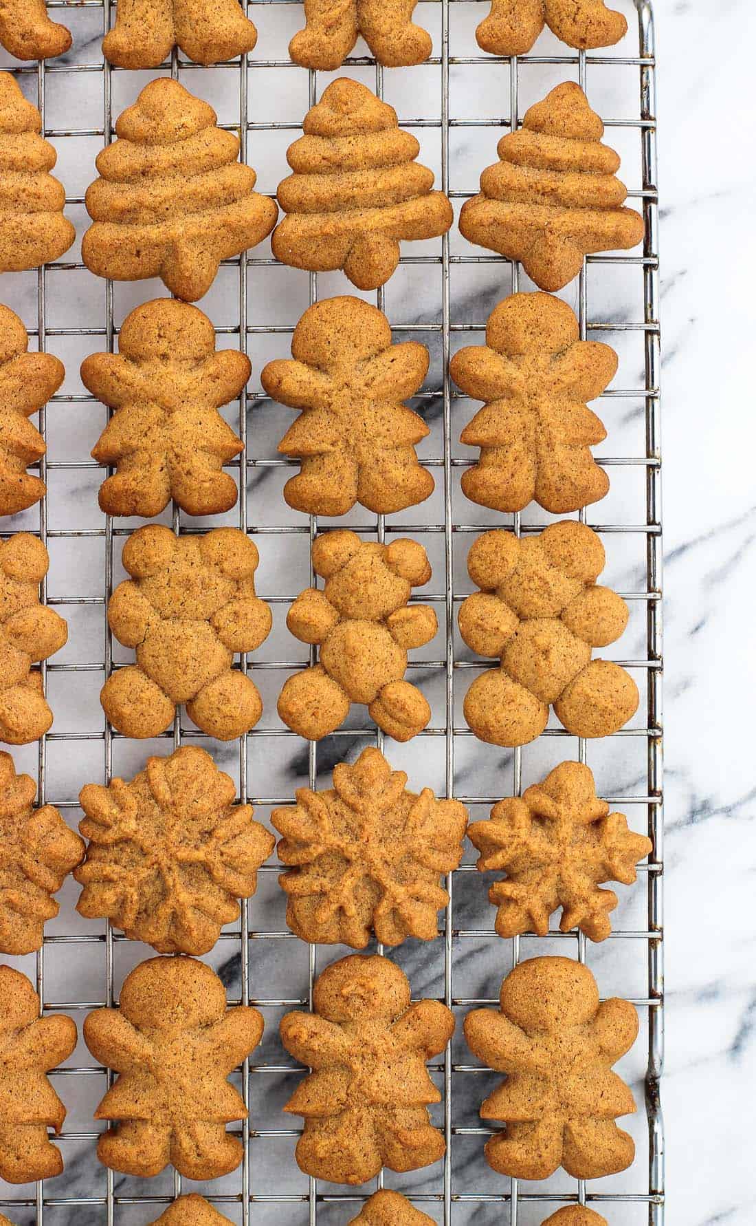 An overhead shot of a variety of gingerbread spritz cookies (a Christmas tree, a gingerbread woman, a teddy bear, and a snowflake) on a wire rack.